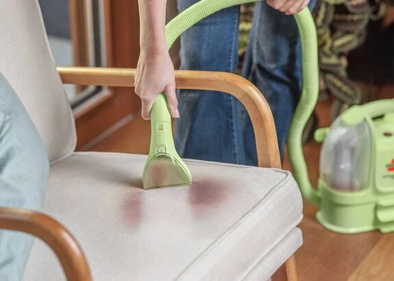Spot-cleaning a stain on an upholstered chair with the BISSELL Little Green Mini