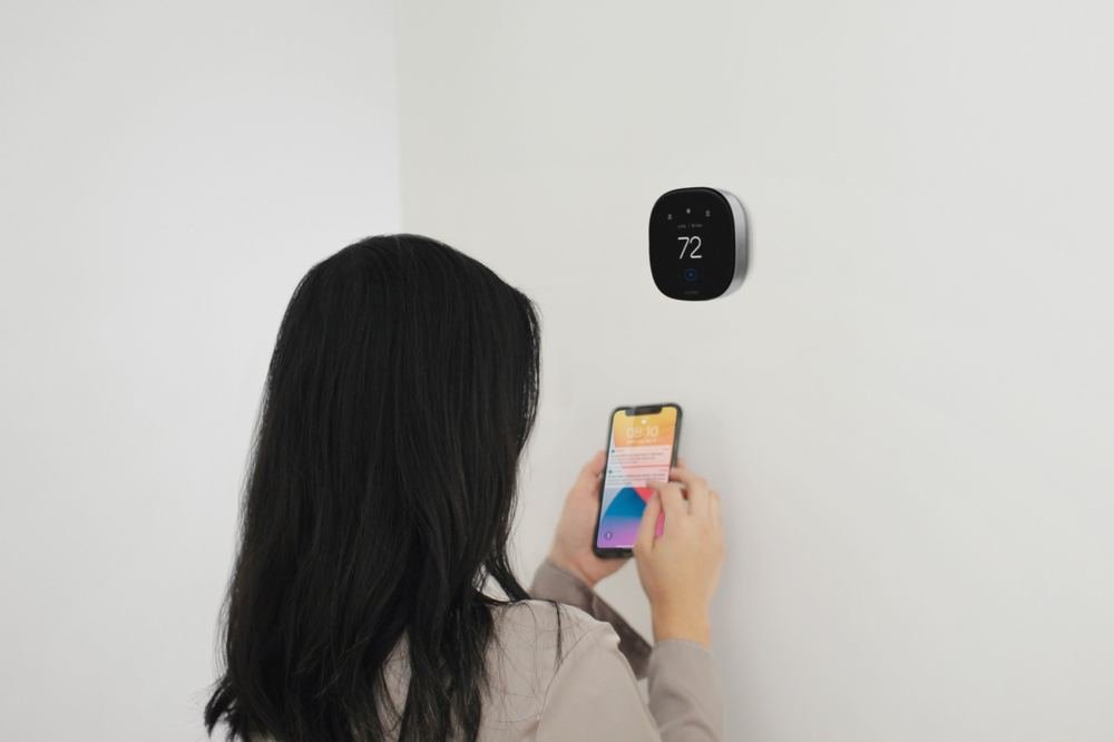 Woman checking the ecobee app on her phone in front of the thermostat